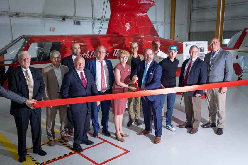 In the centre holding scissors: U.S. Representative Chrissy Houlahan, with Frederick Weyerhaeuser Piaseck (Chairman of the Board and Chief Technology Officer at PiAC) to the left and John Weyerhaeuser Piasecki (President and Chief Executive Officer at PiAC) to the right, also holding scissors.